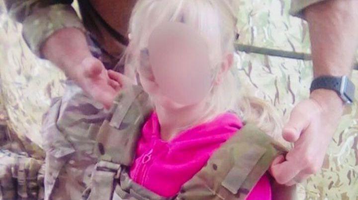 Small child with military body armour being placed on her